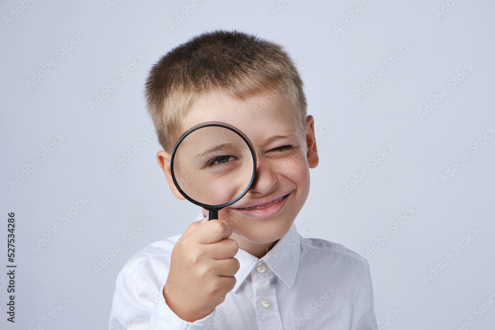 Smiling child looks at the camera through a magnifying glass on a gray background. Close-up.