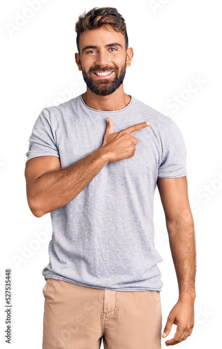 Young hispanic man wearing casual clothes cheerful with a smile on face pointing with hand and finger up to the side with happy and natural expression