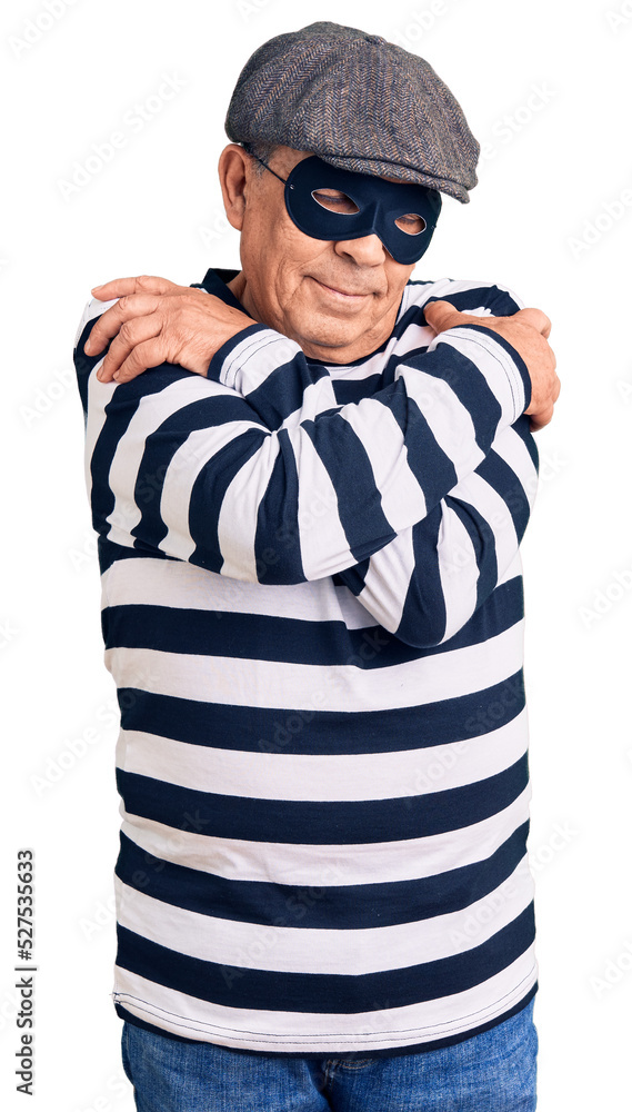 Senior handsome man wearing burglar mask and t-shirt hugging oneself happy and positive, smiling confident. self love and self care Senior handsome man wearing burglar mask and t-shirt hugging oneself happy and positive, smiling confident. self love and self care