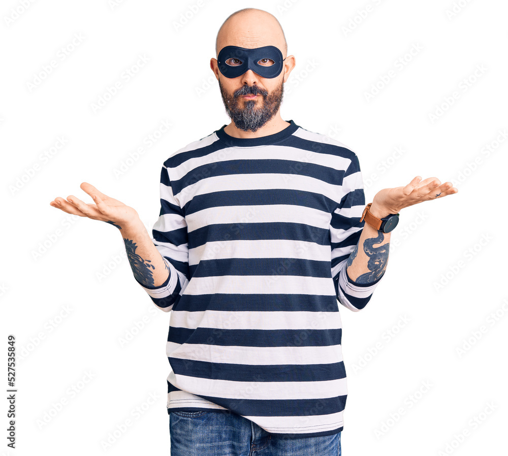 Young handsome man wearing burglar mask clueless and confused with open arms, no idea concept. Young handsome man wearing burglar mask clueless and confused with open arms, no idea concept.
