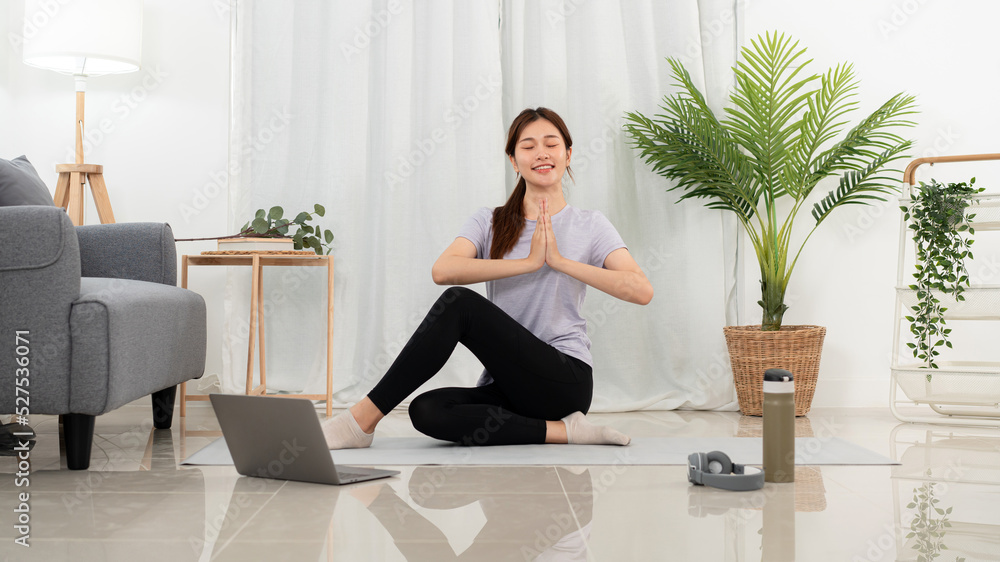 Young woman is relaxing into the lotus position for meditation on mat while taking yoga online class
