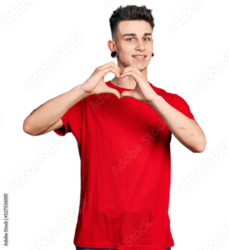Young caucasian boy with ears dilation wearing casual red t shirt smiling in love doing heart symbol shape with hands. romantic concept.