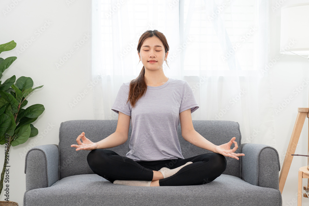 Young woman is relaxing into the lotus position for meditation on couch before workout yoga exercise Young woman is relaxing into the lotus position for meditation on couch before workout yoga exercise