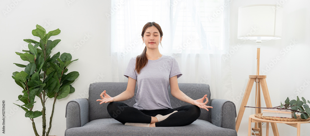 Obraz premium Young woman is relaxing into the lotus position for meditation on couch before workout yoga exercise