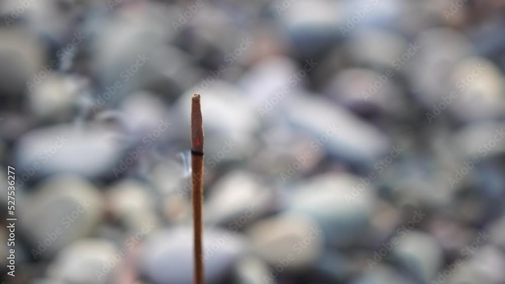 Close up of incense aroma stick burning on the pebble beach sea shore. Small waves on water surface in motion blur with bokeh lights from sunrise. Meditation concept. Close up of incense aroma stick burning on the pebble beach sea shore. Small waves on water surface in motion blur with bokeh lights from sunrise. Meditation concept.