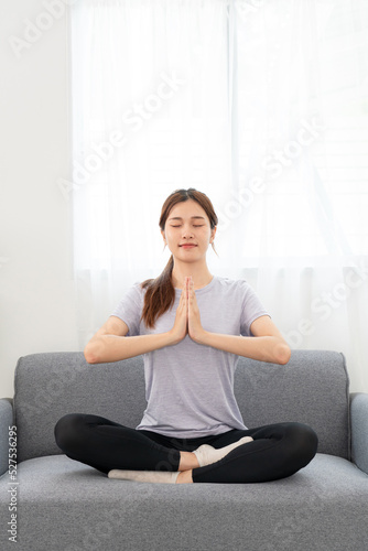 Young woman is relaxing into the lotus position with namaste gesture for meditation on couch