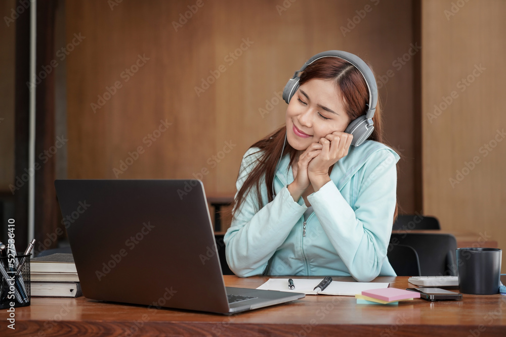 Female student is wearing headphone and sitting to rest your eyes in front of laptop for relaxation Female student is wearing headphone and sitting to rest your eyes in front of laptop for relaxation