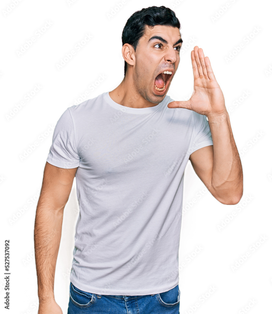 Handsome hispanic man wearing casual white t shirt shouting and screaming loud to side with hand on mouth. communication concept. Handsome hispanic man wearing casual white t shirt shouting and screaming loud to side with hand on mouth. communication concept.