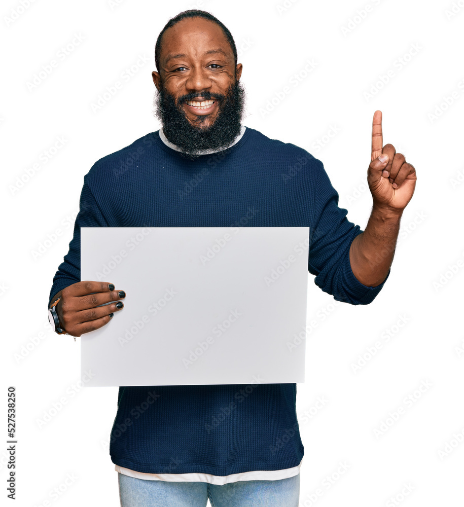 Young african american man holding blank empty banner surprised with an idea or question pointing finger with happy face, number one Young african american man holding blank empty banner surprised with an idea or question pointing finger with happy face, number one
