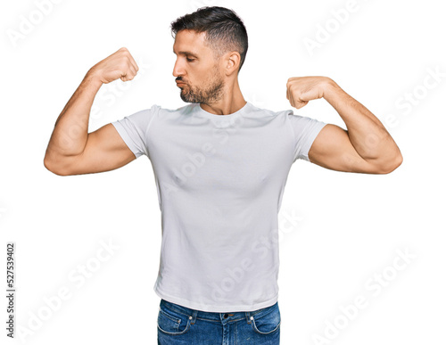 Handsome man with beard wearing casual white t shirt showing arms muscles smiling proud. fitness concept.