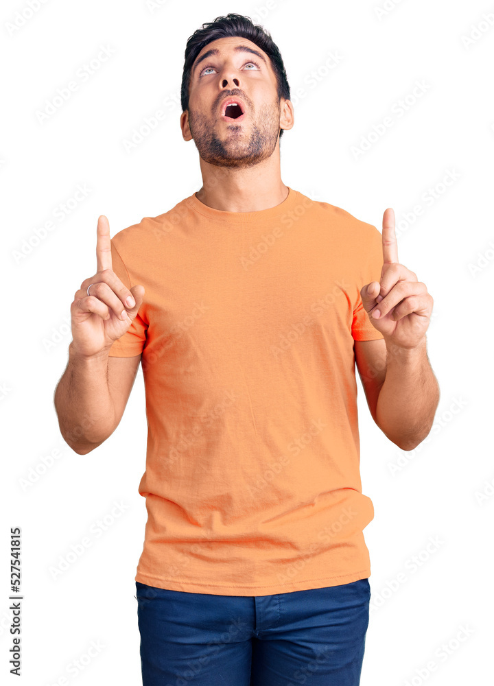 Young hispanic man wearing casual clothes amazed and surprised looking up and pointing with fingers and raised arms. Young hispanic man wearing casual clothes amazed and surprised looking up and pointing with fingers and raised arms.