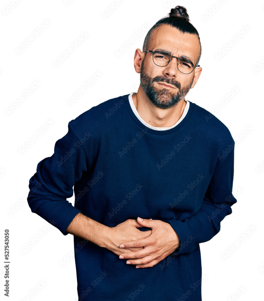 Hispanic man with ponytail wearing casual sweater and glasses with hand on stomach because nausea, painful disease feeling unwell. ache concept. Hispanic man with ponytail wearing casual sweater and glasses with hand on stomach because nausea, painful disease feeling unwell. ache concept.