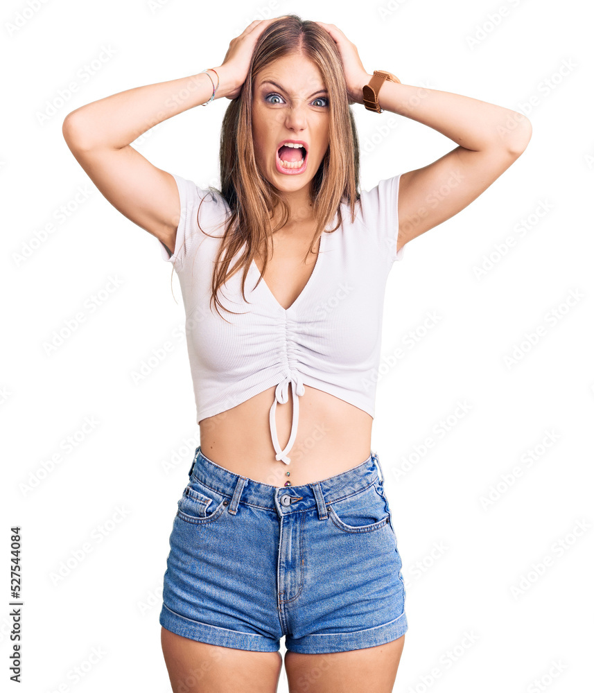 Fototapeta premium Young beautiful blonde woman wearing casual white tshirt crazy and scared with hands on head, afraid and surprised of shock with open mouth
