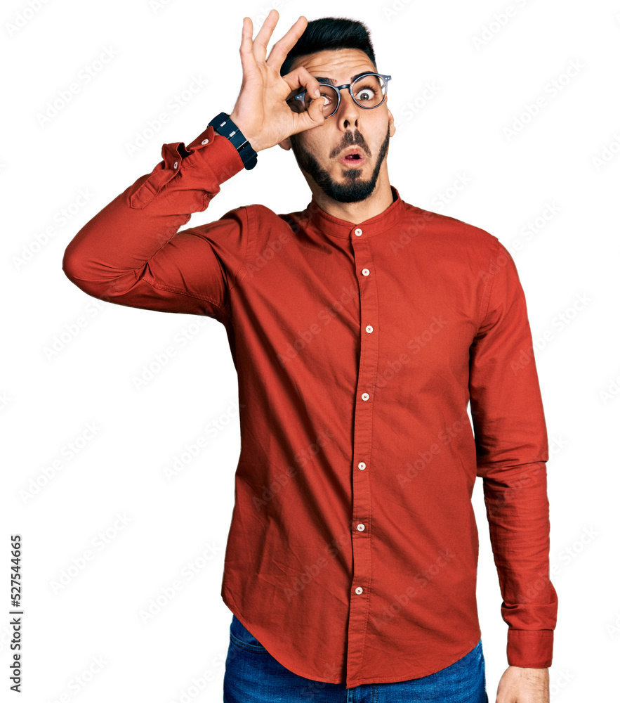 Young hispanic man with beard wearing business shirt and glasses doing ok gesture shocked with surprised face, eye looking through fingers. unbelieving expression. Young hispanic man with beard wearing business shirt and glasses doing ok gesture shocked with surprised face, eye looking through fingers. unbelieving expression.