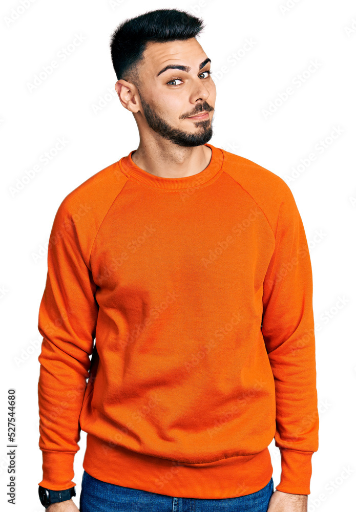 Fototapeta premium Young hispanic man with beard wearing casual orange sweater smiling looking to the side and staring away thinking.