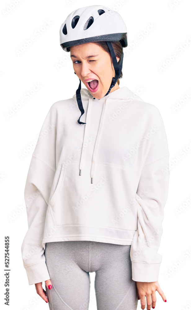 Beautiful brunette young woman wearing bike helmet and sporty clothes winking looking at the camera with sexy expression, cheerful and happy face.