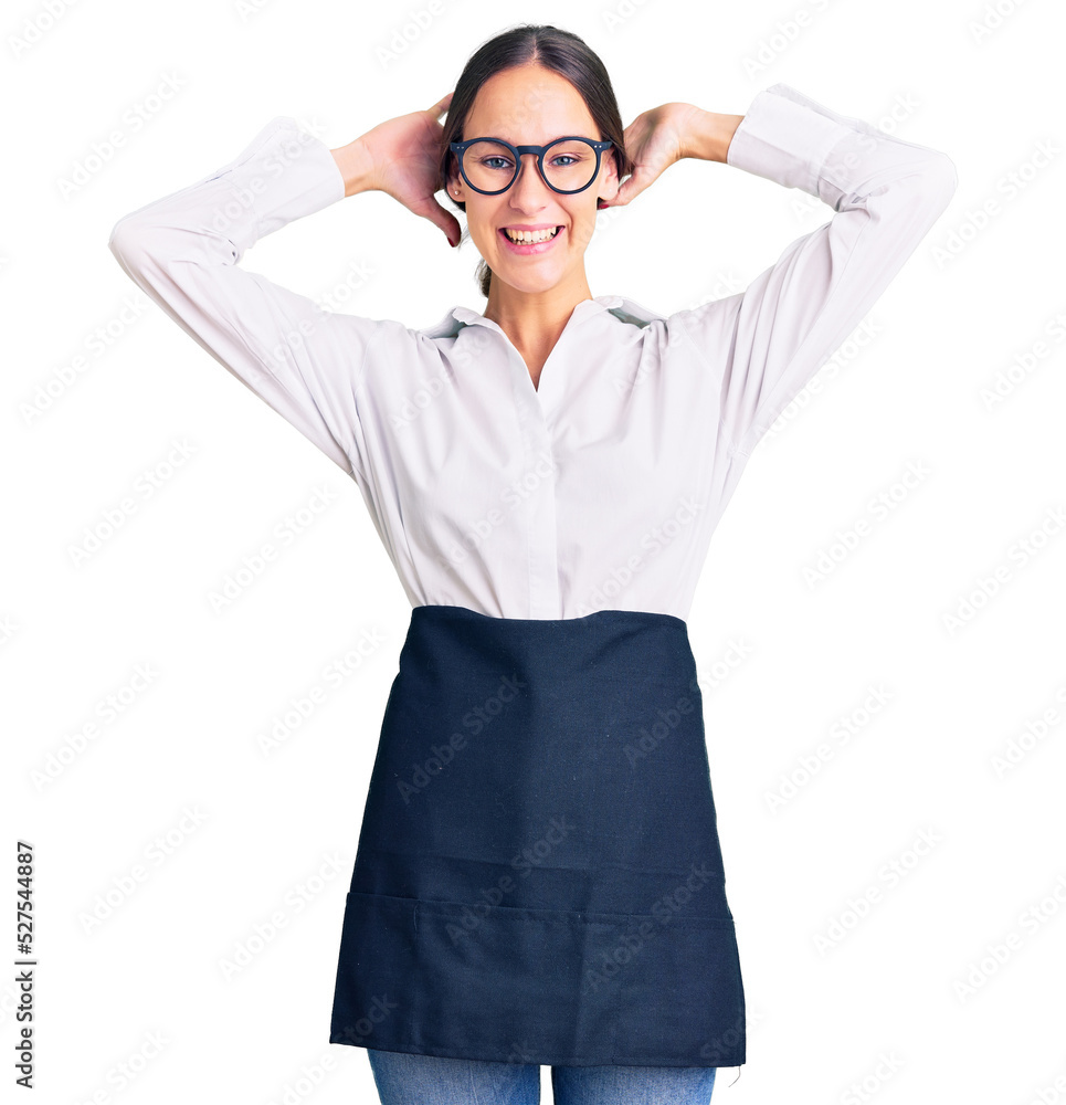 Beautiful brunette young woman wearing professional waitress apron relaxing and stretching, arms and hands behind head and neck smiling happy Beautiful brunette young woman wearing professional waitress apron relaxing and stretching, arms and hands behind head and neck smiling happy