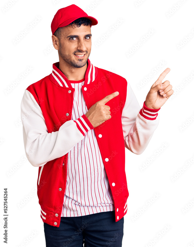 Young hispanic man wearing baseball uniform smiling and looking at the camera pointing with two hands and fingers to the side. Young hispanic man wearing baseball uniform smiling and looking at the camera pointing with two hands and fingers to the side.