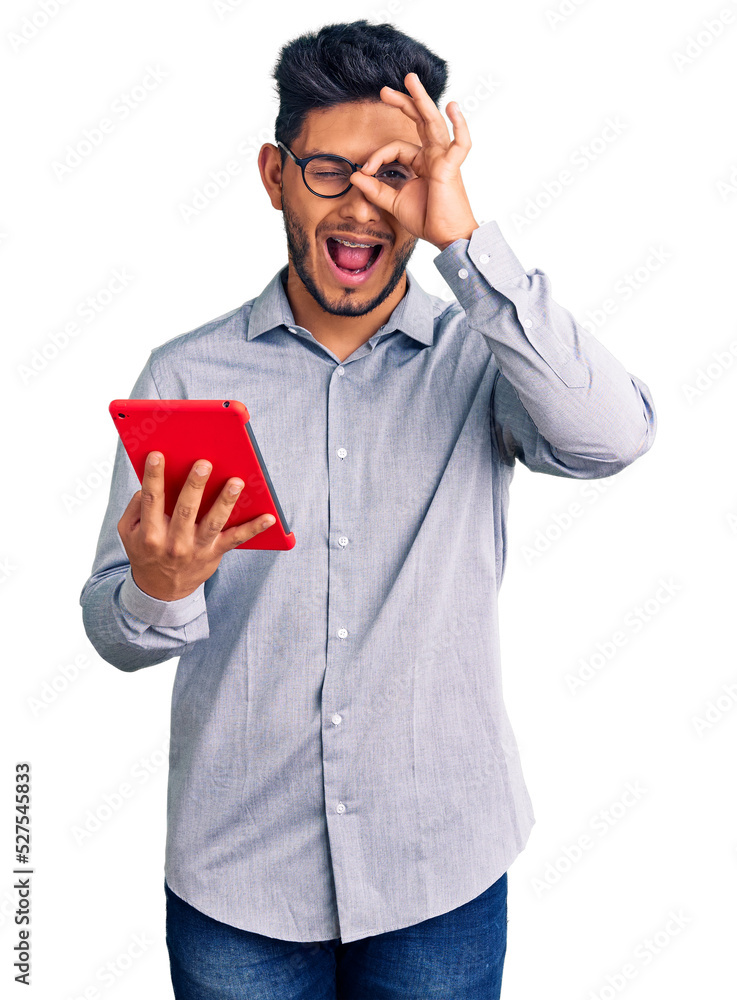 Handsome latin american young man holding touchpad smiling happy doing ok sign with hand on eye looking through fingers