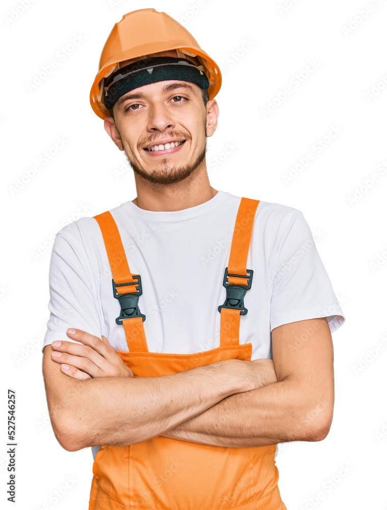 Hispanic young man wearing handyman uniform and safety hardhat happy face smiling with crossed arms looking at the camera. positive person. Hispanic young man wearing handyman uniform and safety hardhat happy face smiling with crossed arms looking at the camera. positive person.