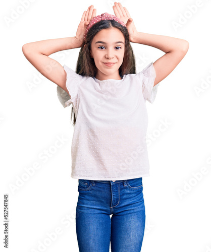 Cute hispanic child girl wearing casual white tshirt doing bunny ears gesture with hands palms looking cynical and skeptical. easter rabbit concept.