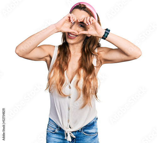 Young caucasian woman wearing casual style with sleeveless shirt doing heart shape with hand and fingers smiling looking through sign