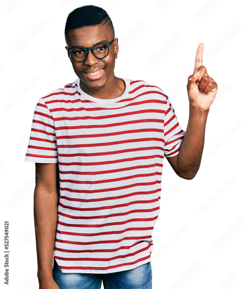 Young african american man wearing casual t shirt and glasses showing and pointing up with finger number one while smiling confident and happy. Young african american man wearing casual t shirt and glasses showing and pointing up with finger number one while smiling confident and happy.