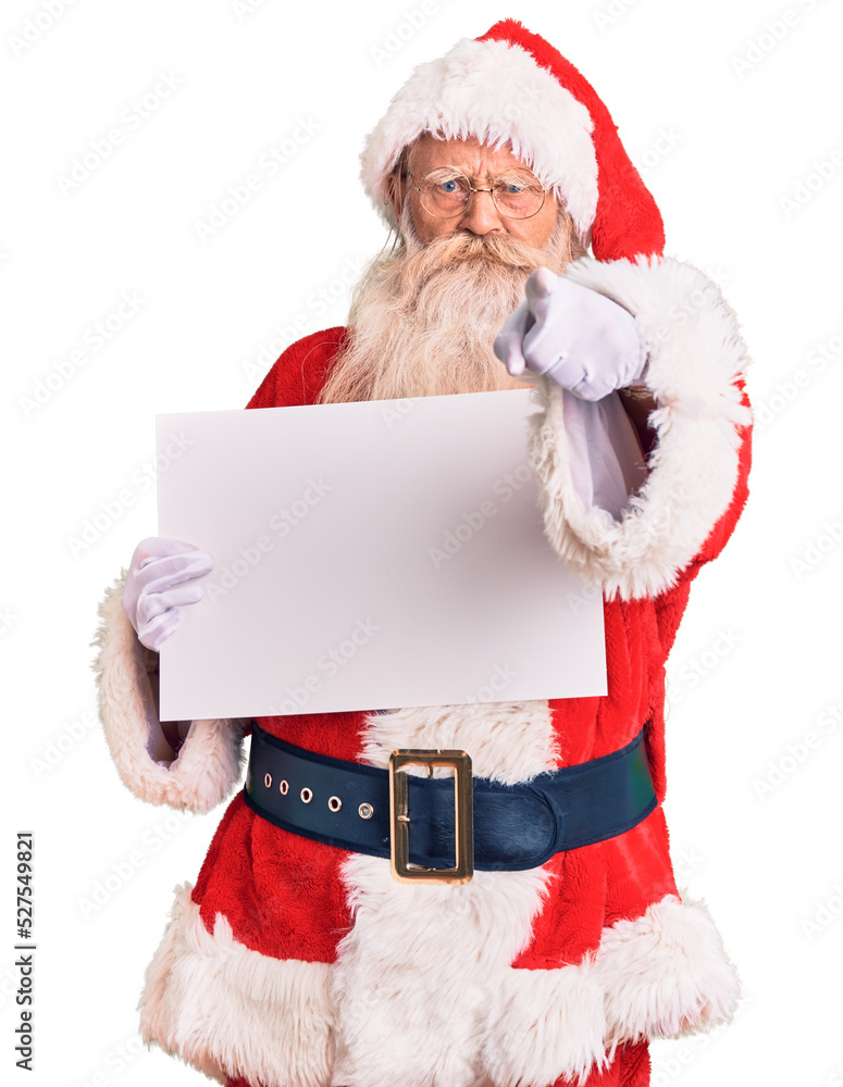 Old senior man with grey hair and long beard wearing santa claus costume holding banner pointing with finger to the camera and to you, confident gesture looking serious Old senior man with grey hair and long beard wearing santa claus costume holding banner pointing with finger to the camera and to you, confident gesture looking serious