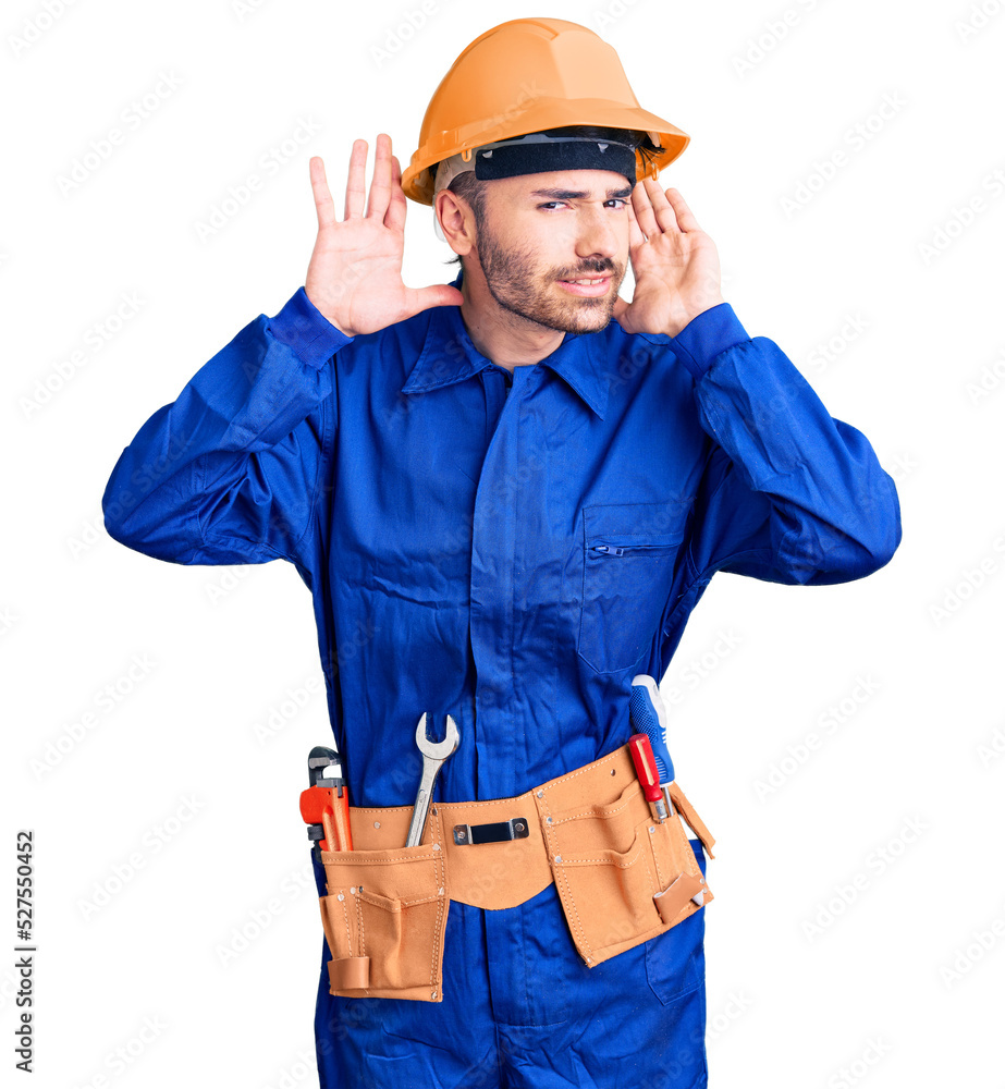 Young hispanic man wearing worker uniform trying to hear both hands on ear gesture, curious for gossip. hearing problem, deaf Young hispanic man wearing worker uniform trying to hear both hands on ear gesture, curious for gossip. hearing problem, deaf
