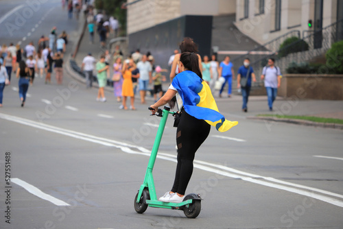 A girl with the flag of Ukraine rides an electric scooter on the road