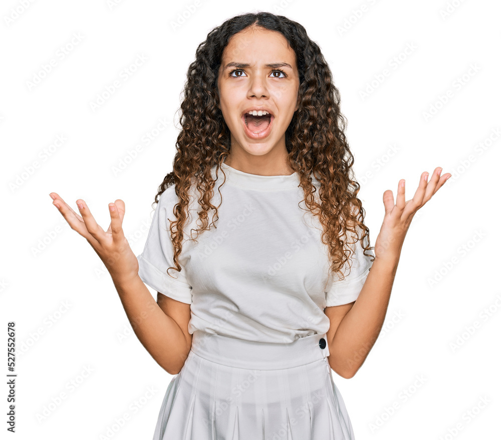 Teenager hispanic girl wearing casual white t shirt crazy and mad shouting and yelling with aggressive expression and arms raised. frustration concept. Teenager hispanic girl wearing casual white t shirt crazy and mad shouting and yelling with aggressive expression and arms raised. frustration concept.