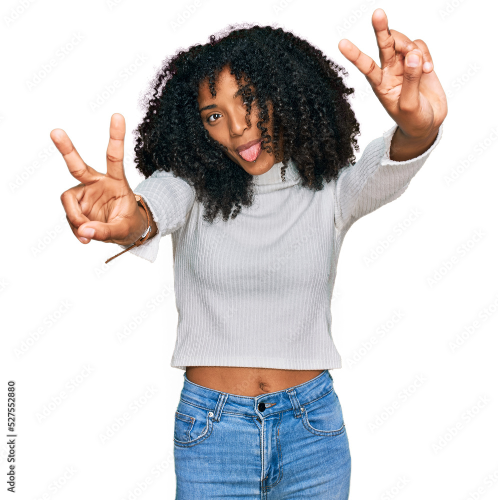 Young african american girl wearing casual clothes smiling with tongue out showing fingers of both hands doing victory sign. number two. Young african american girl wearing casual clothes smiling with tongue out showing fingers of both hands doing victory sign. number two.