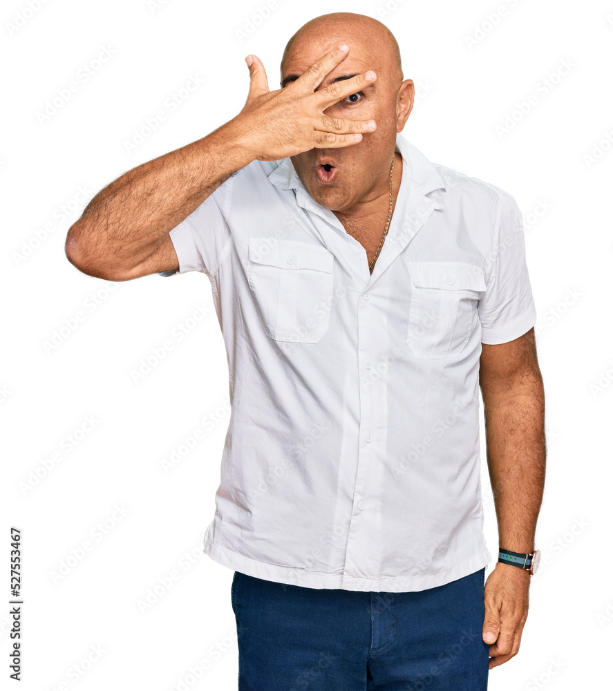 Mature middle east man with mustache wearing casual white shirt peeking in shock covering face and eyes with hand, looking through fingers with embarrassed expression. Mature middle east man with mustache wearing casual white shirt peeking in shock covering face and eyes with hand, looking through fingers with embarrassed expression.