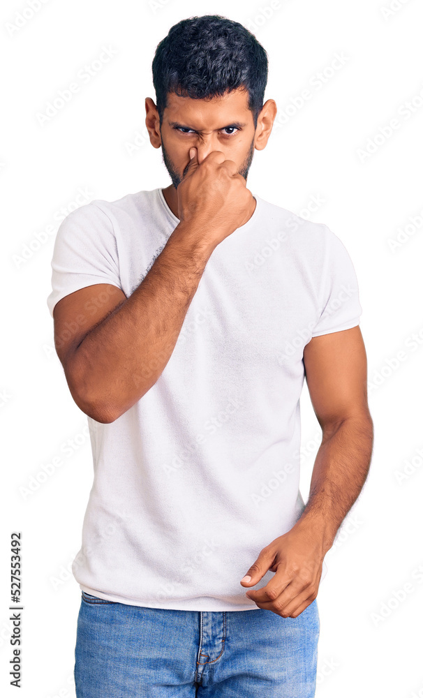 Young latin man wearing casual clothes smelling something stinky and disgusting, intolerable smell, holding breath with fingers on nose. bad smell Young latin man wearing casual clothes smelling something stinky and disgusting, intolerable smell, holding breath with fingers on nose. bad smell