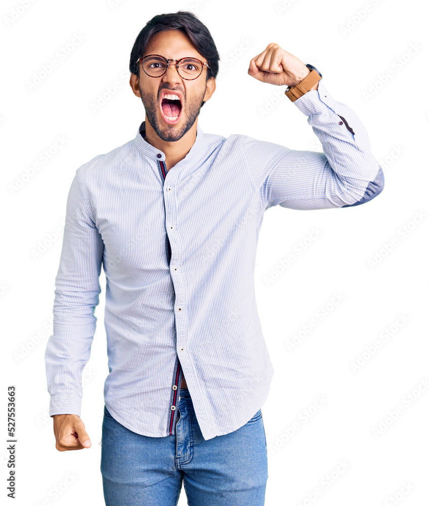 Fototapeta premium Handsome hispanic man wearing business shirt and glasses angry and mad raising fist frustrated and furious while shouting with anger. rage and aggressive concept.