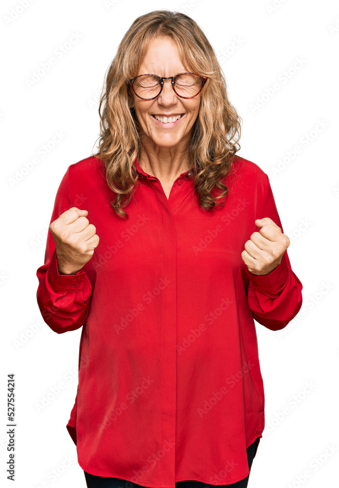 Middle age blonde woman wearing casual shirt over red background very happy and excited doing winner gesture with arms raised, smiling and screaming for success. celebration concept. Middle age blonde woman wearing casual shirt over red background very happy and excited doing winner gesture with arms raised, smiling and screaming for success. celebration concept.