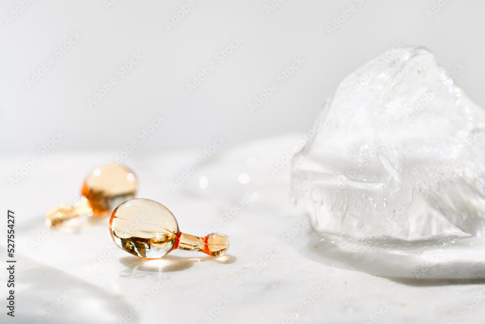 Serum capsules in petri dish for healthy skin with ice balls. Anti-wrinkle rejuvenation skin treatment. Beauty product presentation. Off white stone marble background. Serum capsules in petri dish for healthy skin with ice balls. Anti-wrinkle rejuvenation skin treatment. Beauty product presentation. Off white stone marble background.
