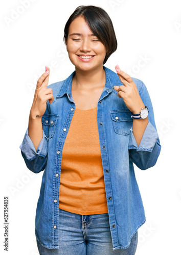 Young beautiful hispanic woman with short hair wearing casual denim jacket gesturing finger crossed smiling with hope and eyes closed. luck and superstitious concept.