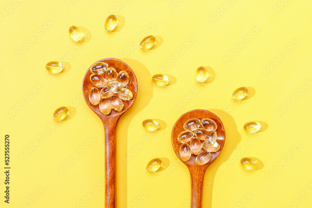 Vitamin D3 capsules on wooden spoons on a yellow background close-up. Vitamin D3 capsules on wooden spoons on a yellow background close-up.