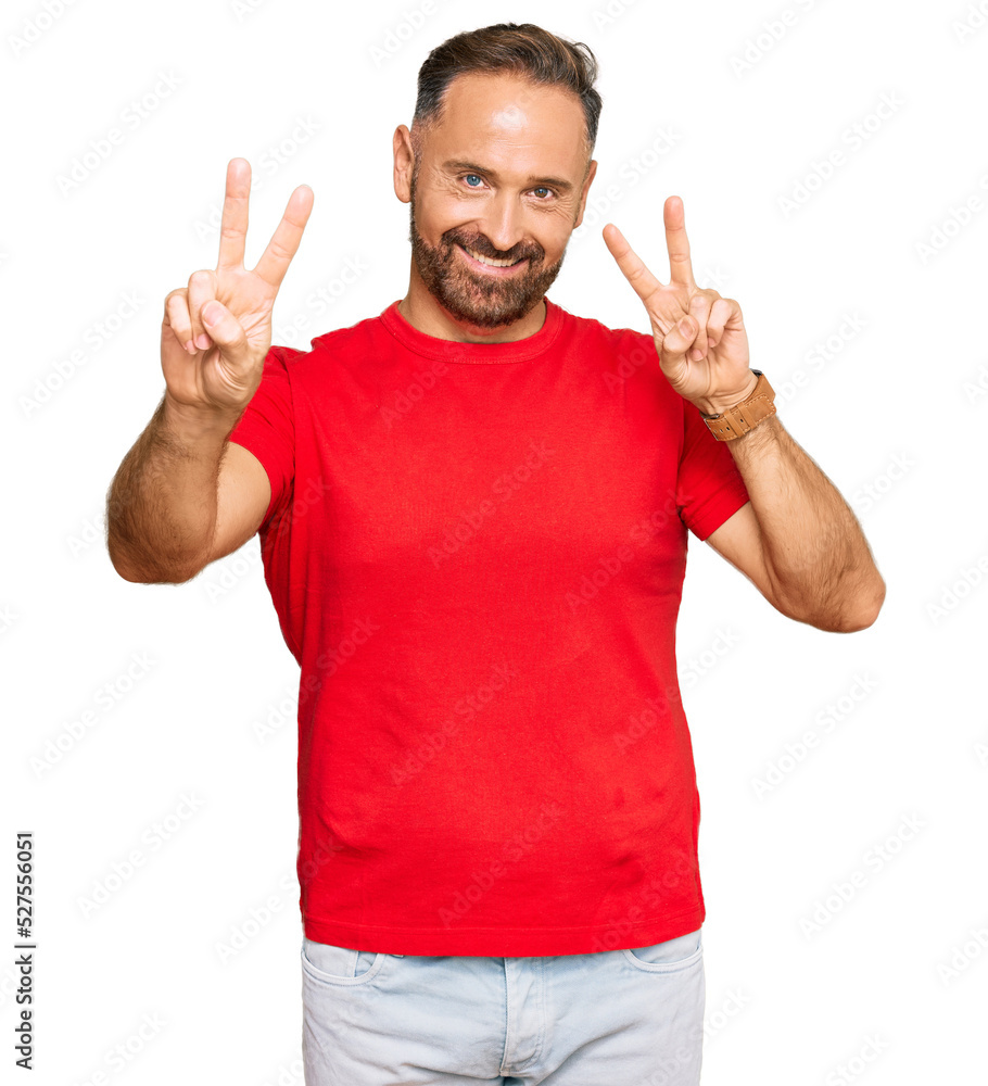 Fototapeta premium Handsome middle age man wearing casual red tshirt smiling looking to the camera showing fingers doing victory sign. number two.