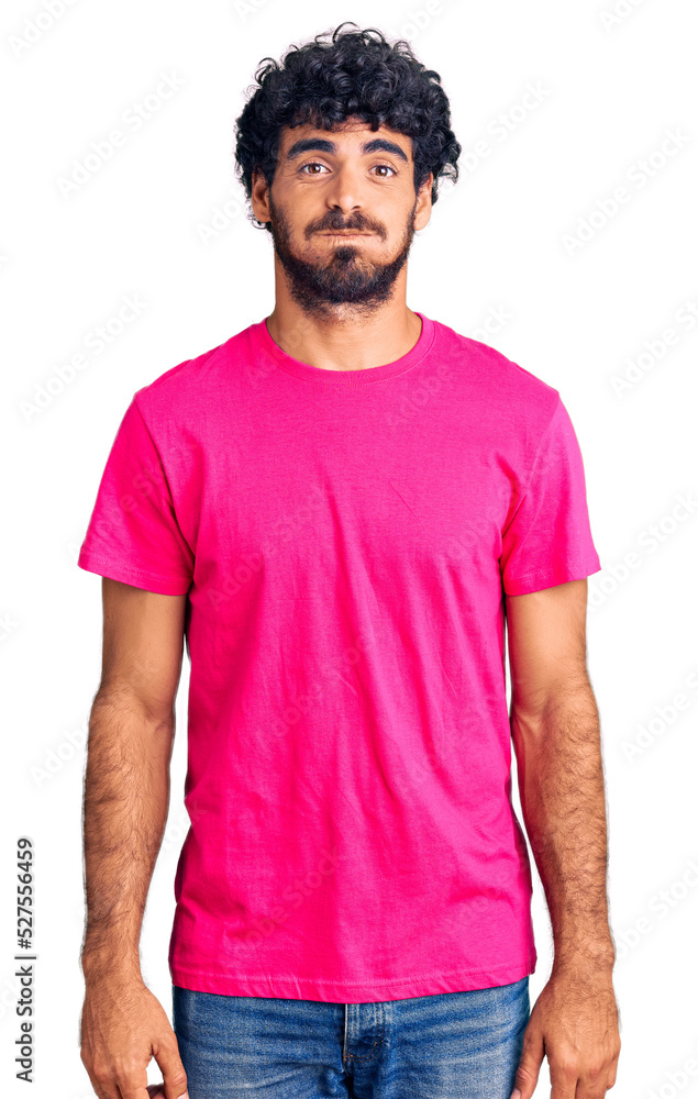 Handsome young man with curly hair and bear wearing casual pink tshirt puffing cheeks with funny face. mouth inflated with air, crazy expression. Handsome young man with curly hair and bear wearing casual pink tshirt puffing cheeks with funny face. mouth inflated with air, crazy expression.
