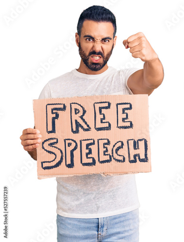 Young hispanic man holding free speech banner annoyed and frustrated shouting with anger, yelling crazy with anger and hand raised