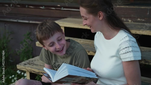 Young mother reads a book with her son sitting on the steps of a country house. Mom and son have fun reading an interesting book. Happy family concept