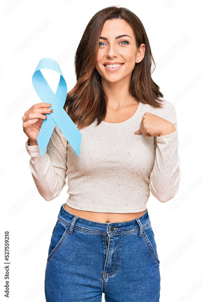 Young brunette woman holding blue ribbon pointing finger to one self smiling happy and proud Young brunette woman holding blue ribbon pointing finger to one self smiling happy and proud