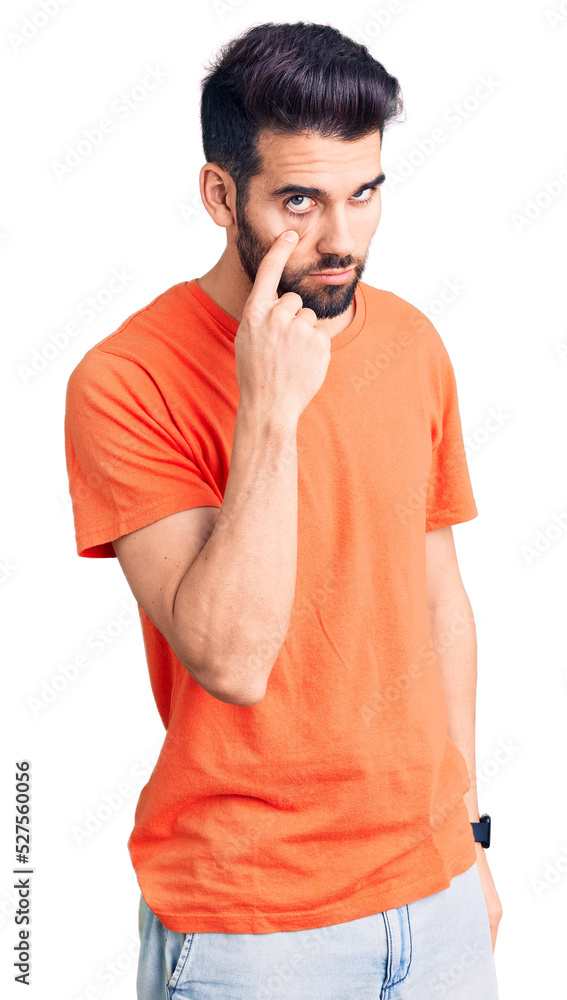 Young handsome man with beard wearing casual t-shirt pointing to the eye watching you gesture, suspicious expression Young handsome man with beard wearing casual t-shirt pointing to the eye watching you gesture, suspicious expression