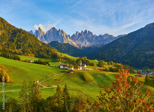 Amazing autumn scenery in Santa Maddalena village with church, colorful trees and meadows under rising sun rays. Dolomite Alps, Italy.