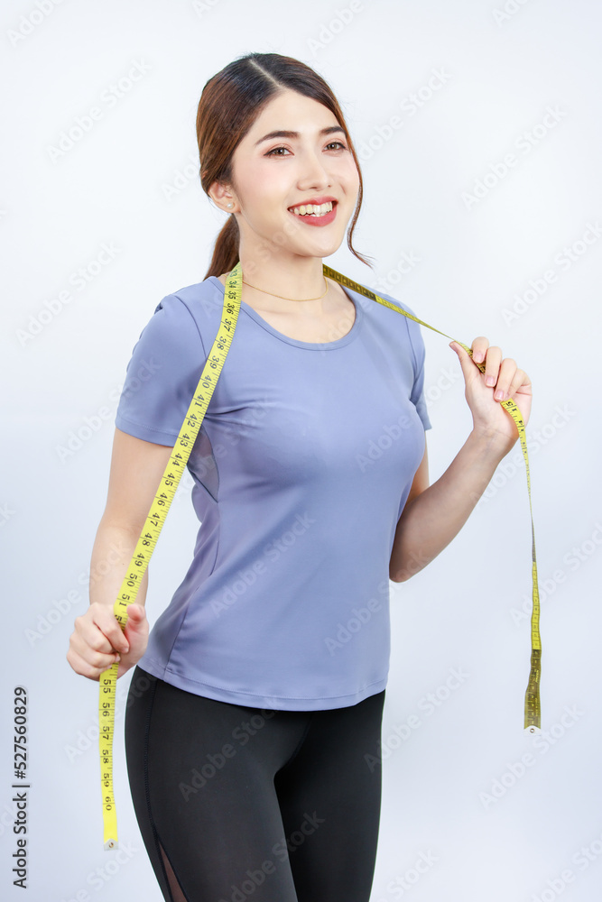 Portrait shot Asian young fit slim female teenager in casual sport wear standing smiling look at camera holding measuring tape around waist after losing weight from exercising on white background Portrait shot Asian young fit slim female teenager in casual sport wear standing smiling look at camera holding measuring tape around waist after losing weight from exercising on white background