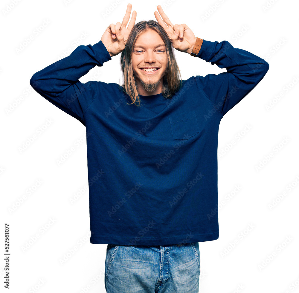 Handsome caucasian man with long hair wearing casual winter sweater posing funny and crazy with fingers on head as bunny ears, smiling cheerful Handsome caucasian man with long hair wearing casual winter sweater posing funny and crazy with fingers on head as bunny ears, smiling cheerful