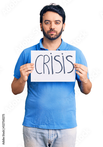Young hispanic man holding crisis message paper thinking attitude and sober expression looking self confident