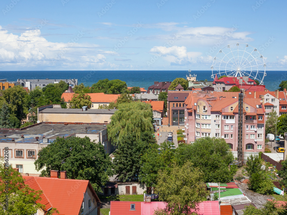 Obraz premium Summer view of tiled roofs, streets with people and ferris wheel ride